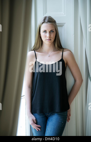 Portrait de jeune femme blonde habillée en passant par l'éclairage naturel grande fenêtre Banque D'Images