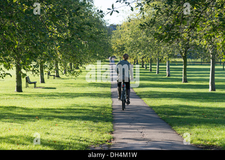 Les cycles d'une femme le long d'un chemin à travers Jésus Green Cambridge UK entre une ligne d'arbres. Banque D'Images