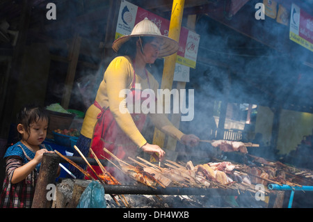 Portrait d'un horizontal dame Lao locale et sa fille griller les brochettes sur un barbecue au bord d'un restaurant. Banque D'Images