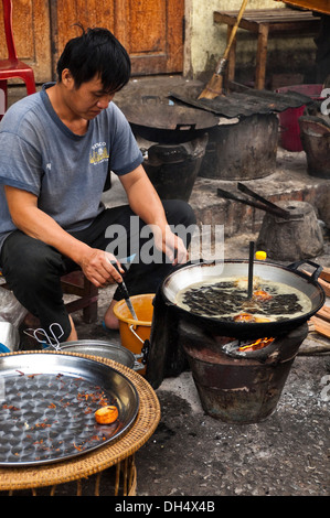 Portrait d'un vertical homme Lao friture petits beignets dans un wok sur la route. Banque D'Images