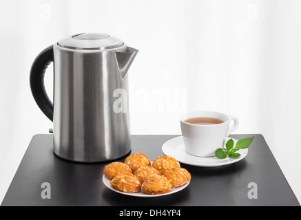 L'heure du thé. Bouilloire électrique, tasse de thé et des cookies sur un tableau noir. Banque D'Images