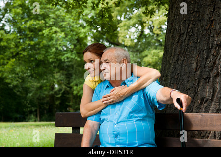 Woman hugging un homme âgé sur un banc dans un parc Banque D'Images