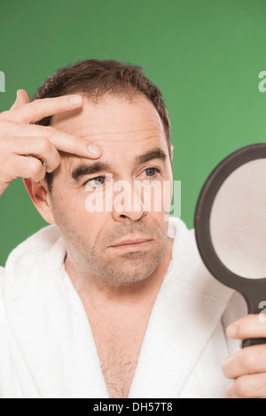 Un homme portant un peignoir d'observer de façon critique lui-même dans un miroir à main, Mannheim, Bade-Wurtemberg, Allemagne Banque D'Images