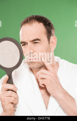 Un homme portant un peignoir d'observer de façon critique lui-même dans un miroir à main, Mannheim, Bade-Wurtemberg, Allemagne Banque D'Images