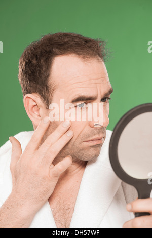 Un homme portant un peignoir d'observer de façon critique lui-même dans un miroir à main, Mannheim, Bade-Wurtemberg, Allemagne Banque D'Images