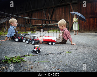 Enfants jouant avec des tracteurs-jouets à la ferme, Reith im Alpbachtal, district de Kufstein, Tyrol du Nord, Tirol, Autriche Banque D'Images