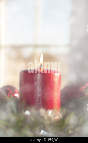 L'image de rêve d'une bougie de Noël rouge brûlant à l'intérieur une couronne, avec une fenêtre sur l'arrière-plan Banque D'Images