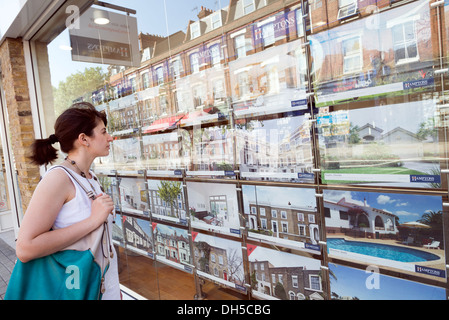 Jeune femme à la recherche de maisons à vendre dans la fenêtre de l'agent immobilier, Islington, Londres, Royaume-Uni Banque D'Images