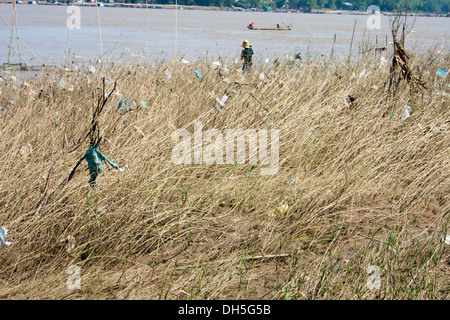 Un pêcheur est la pêche, près de sacs en plastique qui ont rassemblé dans les mauvaises herbes sur la rive du Mékong dans la région de Kampong Cham, au Cambodge. Banque D'Images