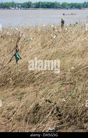 Un pêcheur est la pêche, près de sacs en plastique qui ont rassemblé dans les mauvaises herbes sur la rive du Mékong dans la région de Kampong Cham, au Cambodge. Banque D'Images