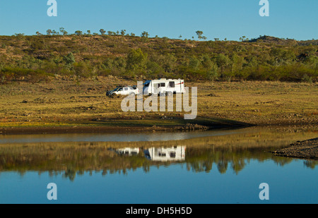 Caravane blanche et voiture / véhicule stationné sur une colline herbeuse reflète dans l'eau du lac bleu - Corella outback Queensland Banque D'Images