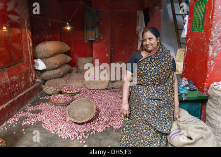 Femme marché debout devant sa boutique, sacs de jute remplie d'oignons à l'arrière, le marché aux épices, Vieux Dhaka, Dhaka, Bangladesh Banque D'Images