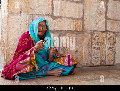 Personnes âgées femme portant un sari indien assis sur le sol devant un temple indou jouant des cymbales pour la prière, don de pièces Banque D'Images