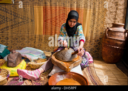 Femme berbère assis sur le poncer à grains d'argan de la pâte pour la préparation de l'huile d'argan, Anti-Atlas Atlas ou moins Banque D'Images