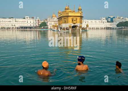 Temple d'or, Hari Mandir, le temple principal de la religion Sikh, trois pèlerins portant des turbans de prendre un bain rituel dans le lac sacré de Banque D'Images