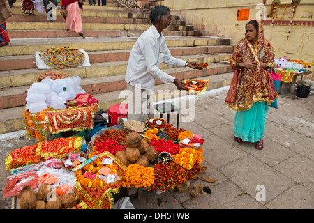 L'homme à un étal proposant des petits bols avec des fleurs et des offrandes rituelles à une femme qui passe, les bols sont offerts en sacrifice Banque D'Images