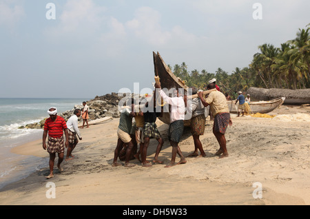 Les pêcheurs poussant leur bateau de l'eau sur la plage, Varkala, Kerala, Inde, Asie Banque D'Images