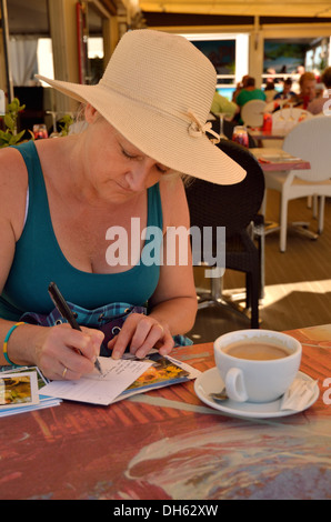 Femme mature sur l'écriture de cartes postales dans un café français Banque D'Images