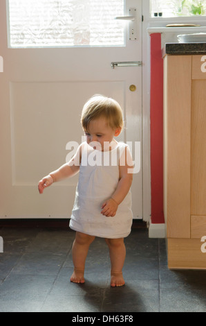 Fille de 9 mois, apprendre à se lever et marcher sur plancher de la cuisine. Angleterre, Royaume-Uni. Banque D'Images