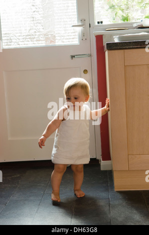 Fille de 9 mois, apprendre à se lever et marcher sur plancher de la cuisine. Angleterre, Royaume-Uni. Banque D'Images