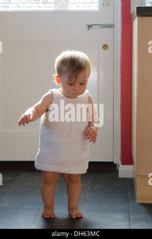 Fille de 9 mois, apprendre à se lever et marcher sur plancher de la cuisine. Angleterre, Royaume-Uni. Banque D'Images