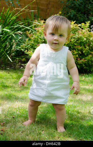 Fille de 9 mois, apprendre à se lever et à marcher sur l'herbe dans le jardin. Angleterre, Royaume-Uni. Banque D'Images