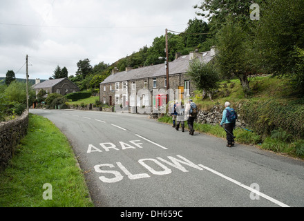 Bilingue anglais et gallois signe lent l'ARAF peints sur la route principale avec des promeneurs marchant dans village. Betws Garmon Gwynedd au Pays de Galles Banque D'Images