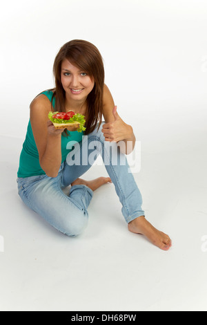 Jeune femme avec grain pain garni de fromage et de tomate, thumbs-up Banque D'Images