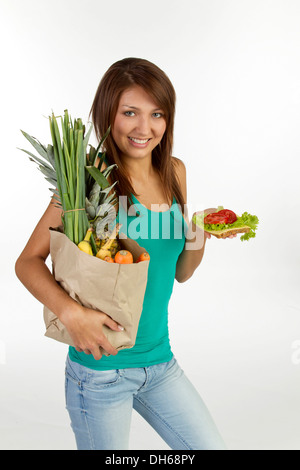 Jeune femme avec grain pain garni avec du fromage et de la tomate et un sac de fruits et légumes Banque D'Images