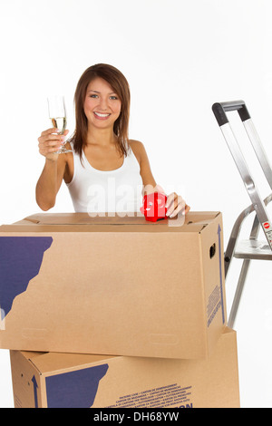 Jeune femme avec des cartons, une tirelire et un verre de champagne dans sa main Banque D'Images