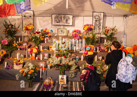 New York, NY, 31 octobre 2013. Une femme et un garçon se tenir en face de l'autel du public dans une tente à l'extérieur de l'église de Saint Marc-dans-le-Bowery à New York City's Lower East Side. Les illustrations en noir et blanc sur le mur arrière sont des répliques d'illustrations de José Guadalupe Posada, créateur de la catrina, le crâne de la femme vu dans l'illustration de gauche. Credit : Ed Lefkowicz/Alamy Live News Banque D'Images