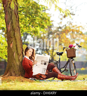 Jeune femme assise sur un vélo avec de l'herbe verte et de lire le journal dans un parc Banque D'Images