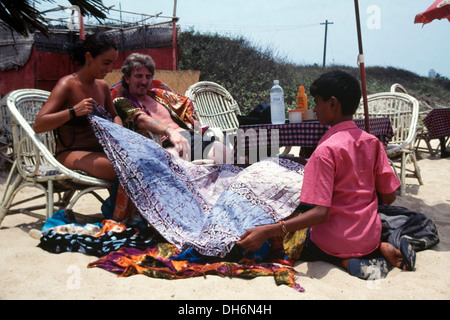 Garçon qui tentait de vendre un sarong à couple de touristes sur la plage de benaulim goa inde Banque D'Images