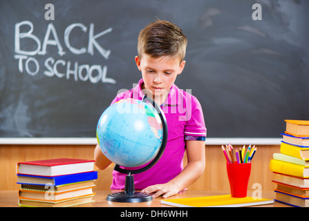 Cute schoolboy à sur globe in classroom Banque D'Images