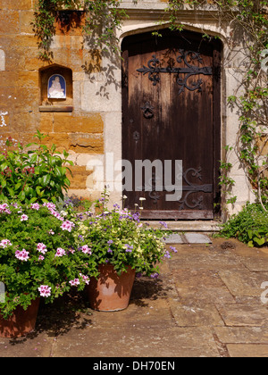 Vieille porte en chêne foncé dans un mur de l'Ironstone, Coton Manor, Coton, Northamptonshire, Angleterre. Banque D'Images