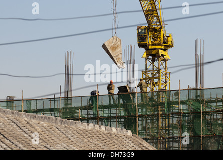 Les constructeurs qui utilisent une grue pour charger du ciment sur un chantier de construction à Pékin, tout en travaillant à construire un nouveau bâtiment soutenu par des échafaudages. © Olli Geibel Banque D'Images