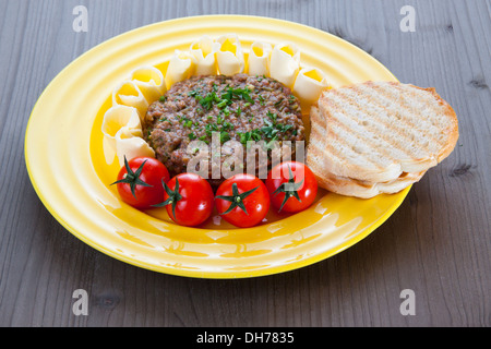 Steak tartare avec du pain grillé, des tomates et du beurre sur la plaque jaune Banque D'Images