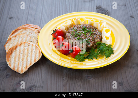 Steak tartare avec du pain grillé, des tomates et du beurre sur la plaque jaune Banque D'Images