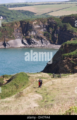 Couple en train de marcher le long du sentier côtier avec la mer bleue et les falaises en arrière-plan. Banque D'Images