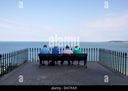 Quatre personnes s'assit sur un banc avec vue sur la mer. Banque D'Images