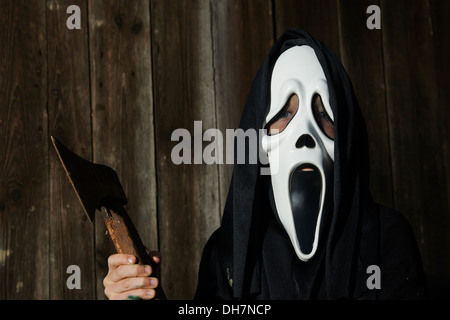 Dans l'homme effrayant 'scream' mask est titulaire d'ax. Masque de la grande faucheuse. Blanc carnaval masque fantôme noir et capot. Scary Movie film. Banque D'Images