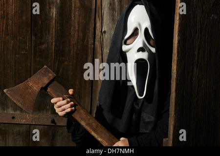 Dans l'homme effrayant 'scream' mask est titulaire d'ax. Masque de la grande faucheuse. Blanc carnaval masque fantôme noir et capot. Scary Movie film. Banque D'Images