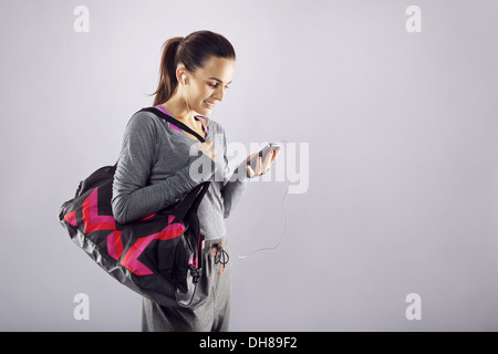 Bon à la femme athlète avec un sac de sport à l'écoute de la musique sur son téléphone mobile. Femme de remise en forme dans les vêtements de sport Banque D'Images
