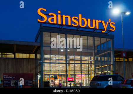 Un grand supermarché Sainsbury's avec le signe sur le toit éclairés la nuit. Banque D'Images