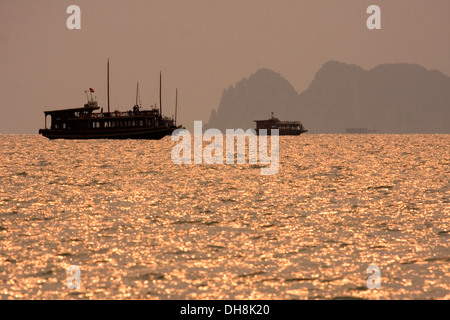 En bois traditionnelles vietnamiennes, les bateaux naviguent dans la baie de Halong au coucher du soleil, le Vietnam. Banque D'Images