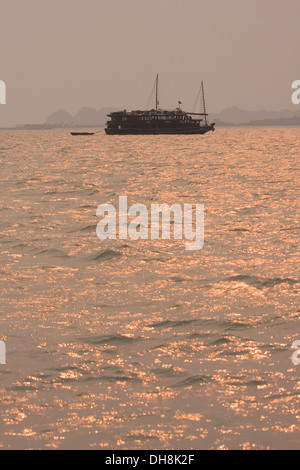 En bois traditionnelles vietnamiennes, les bateaux naviguent dans la baie de Halong au coucher du soleil, le Vietnam. Banque D'Images