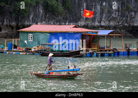 Pêcheur en barque devant les maisons flottantes dans la baie d'Halong. Banque D'Images