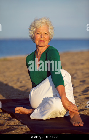 Senior woman yoga sur la plage au matin. Vieille Femme faisant des exercices d'étirement sur la plage. Banque D'Images