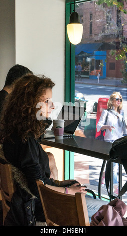 Jolie jeune femme assise au comptoir Starbucks montres fenêtre passants comme homme à côté de ses œuvres sur son ordinateur New York City Banque D'Images