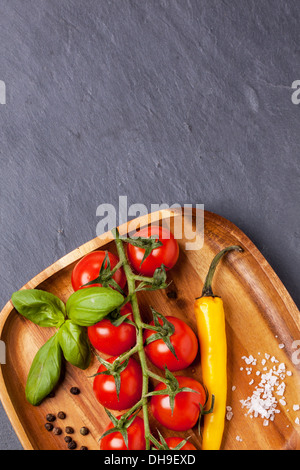 Vue de dessus sur les tomates cerises, piment et basilic avec du sel et du poivre sur la plaque en bois sur fond gris foncé Banque D'Images